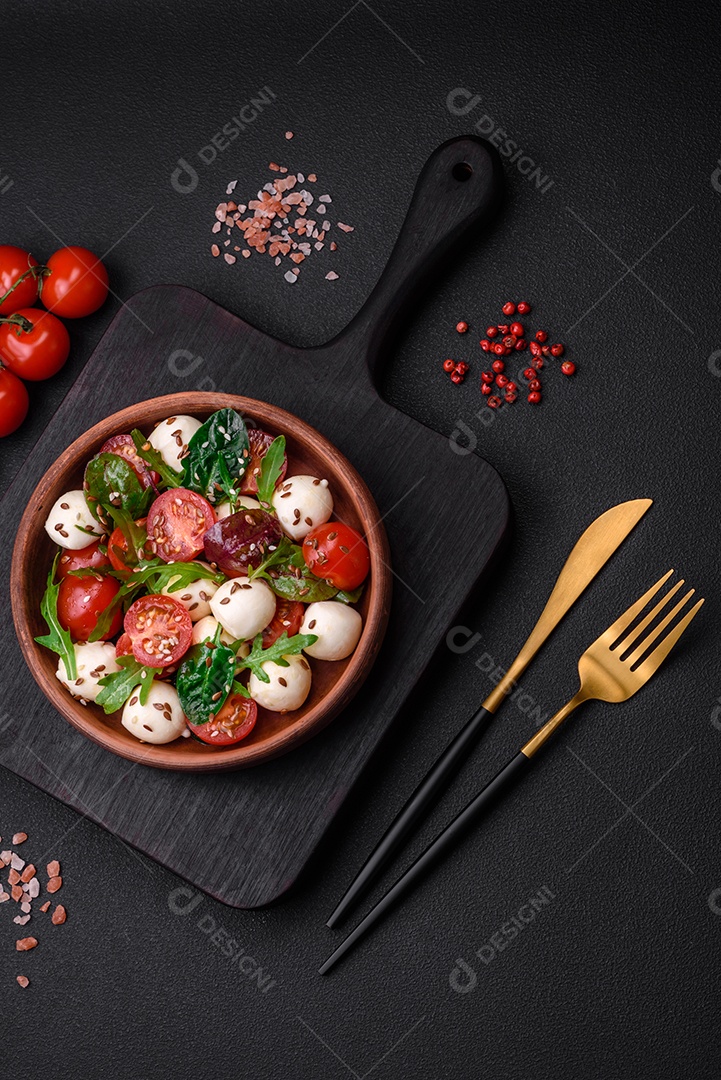 Deliciosa salada fresca com queijo mussarela, tomate cereja, ervas, sal e especiarias sobre um fundo escuro de concreto