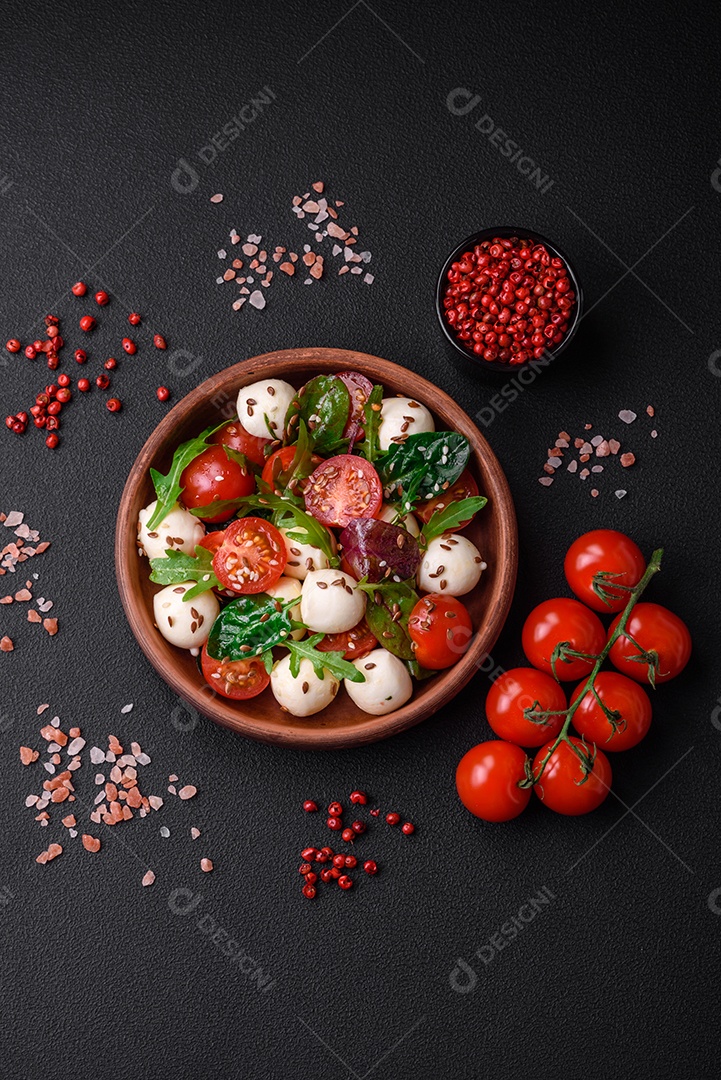 Deliciosa salada fresca com queijo mussarela, tomate cereja, ervas, sal e especiarias sobre um fundo escuro de concreto