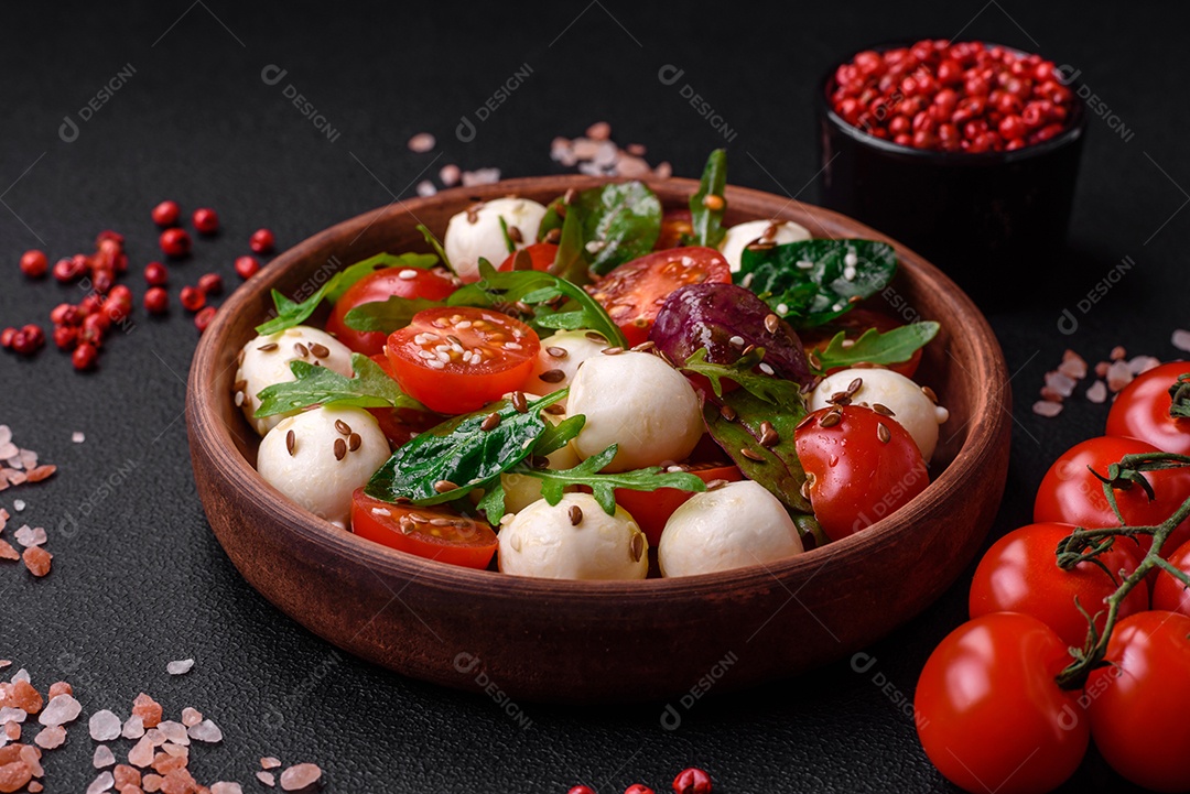 Deliciosa salada fresca com queijo mussarela, tomate cereja, ervas, sal e especiarias sobre um fundo escuro de concreto