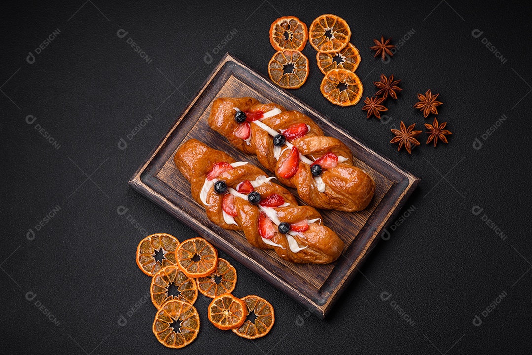 Deliciosa massa crocante fresca em forma de trança com morangos e mirtilos sobre um fundo escuro de concreto