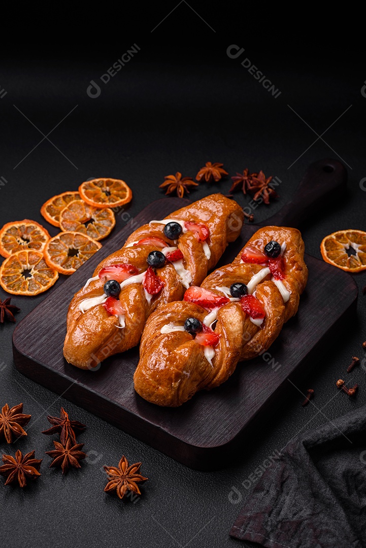 Deliciosa massa crocante fresca em forma de trança com morangos e mirtilos sobre um fundo escuro de concreto