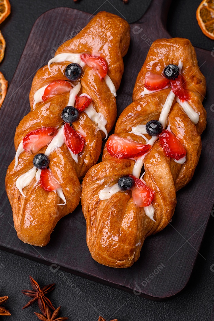 Deliciosa massa crocante fresca em forma de trança com morangos e mirtilos sobre um fundo escuro de concreto