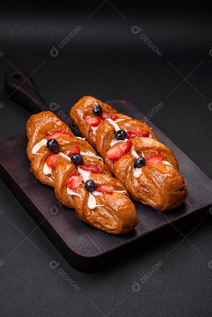 Deliciosa massa crocante fresca em forma de trança com morangos e mirtilos sobre um fundo escuro de concreto