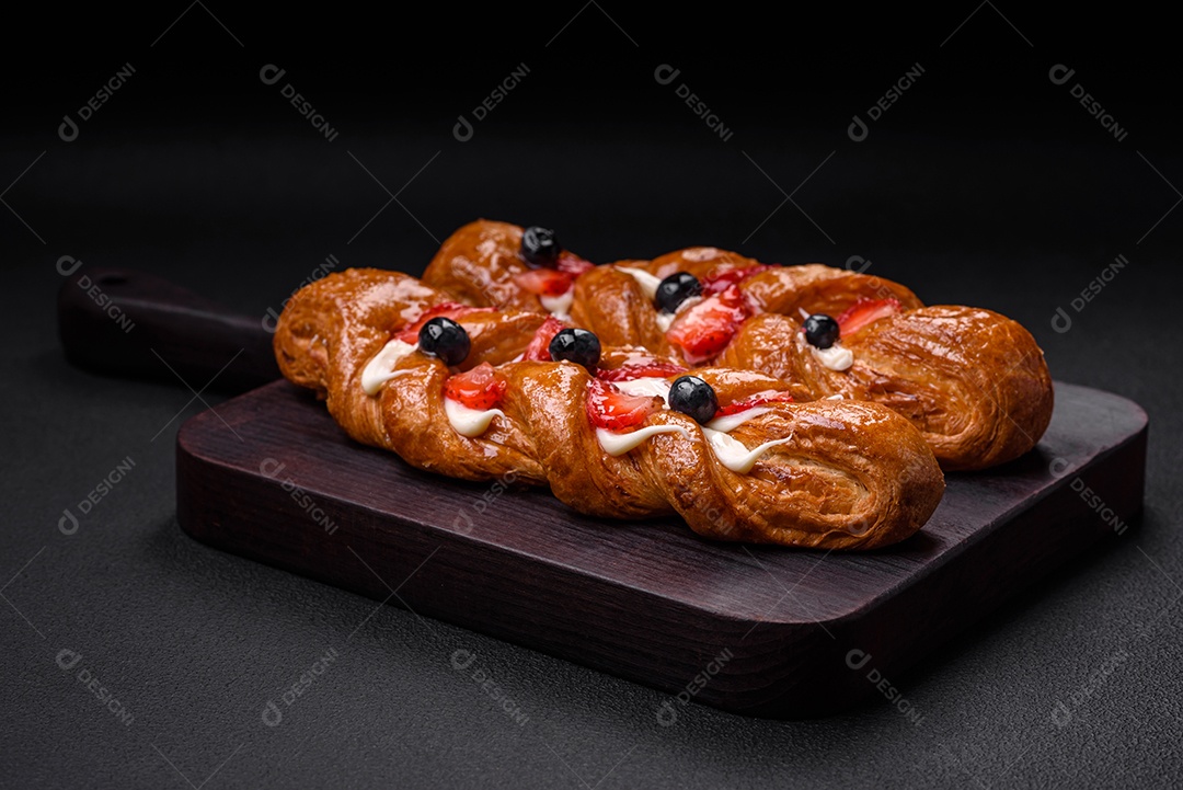 Deliciosa massa crocante fresca em forma de trança com morangos e mirtilos sobre um fundo escuro de concreto