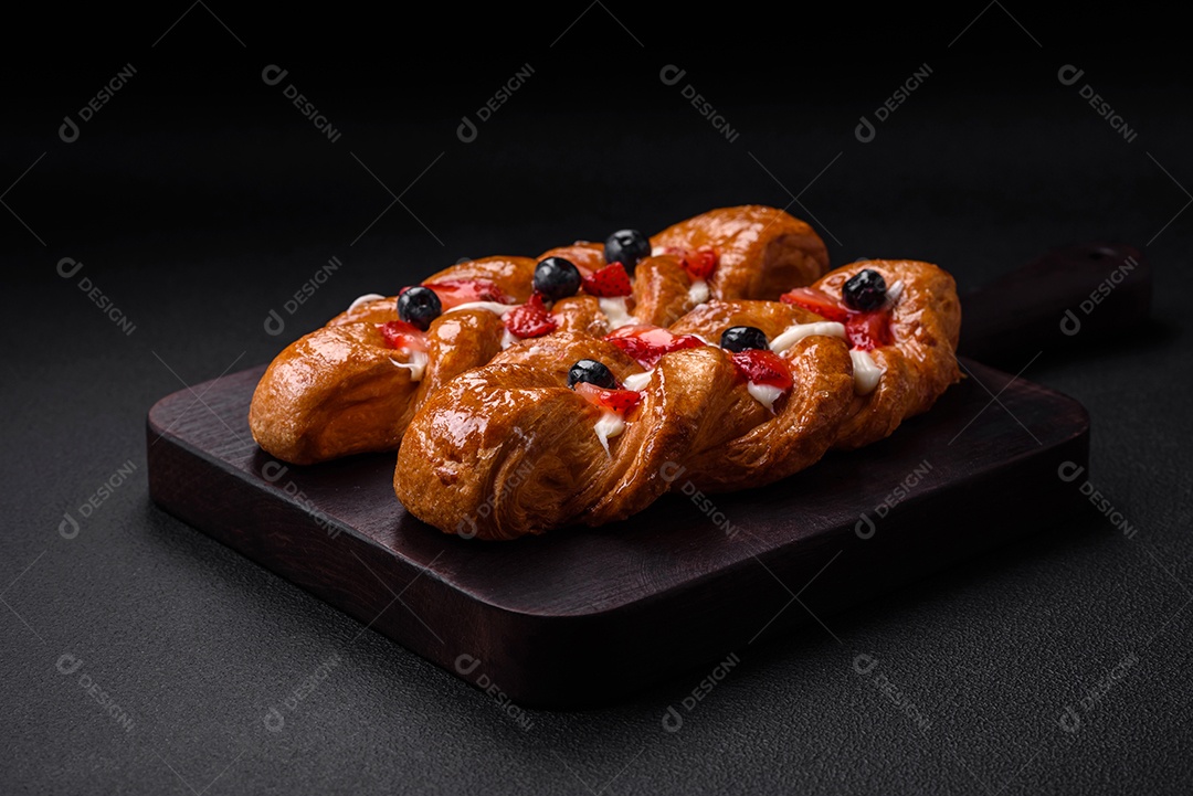 Deliciosa massa crocante fresca em forma de trança com morangos e mirtilos sobre um fundo escuro de concreto