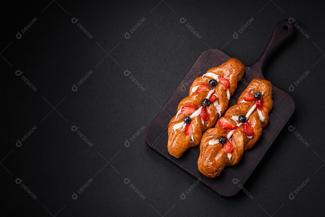 Deliciosa massa crocante fresca em forma de trança com morangos e mirtilos sobre um fundo escuro de concreto