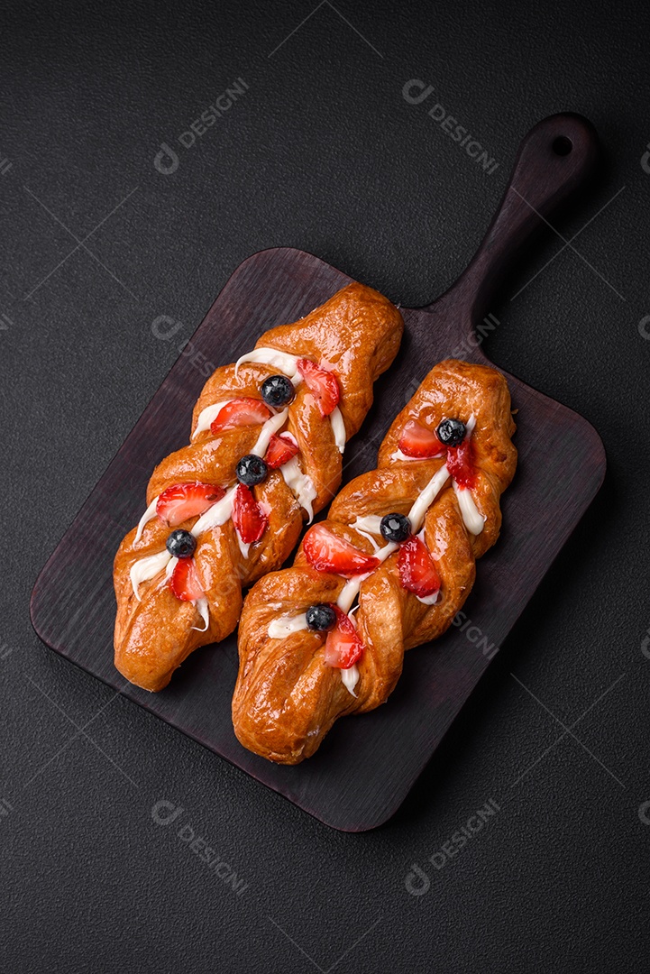 Deliciosa massa crocante fresca em forma de trança com morangos e mirtilos sobre um fundo escuro de concreto