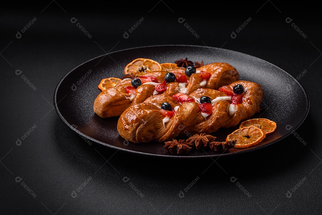 Deliciosa massa crocante fresca em forma de trança com morangos e mirtilos sobre um fundo escuro de concreto