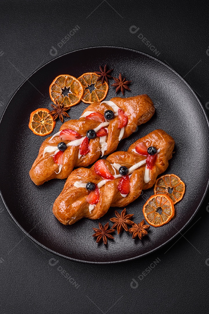 Deliciosa massa crocante fresca em forma de trança com morangos e mirtilos sobre um fundo escuro de concreto