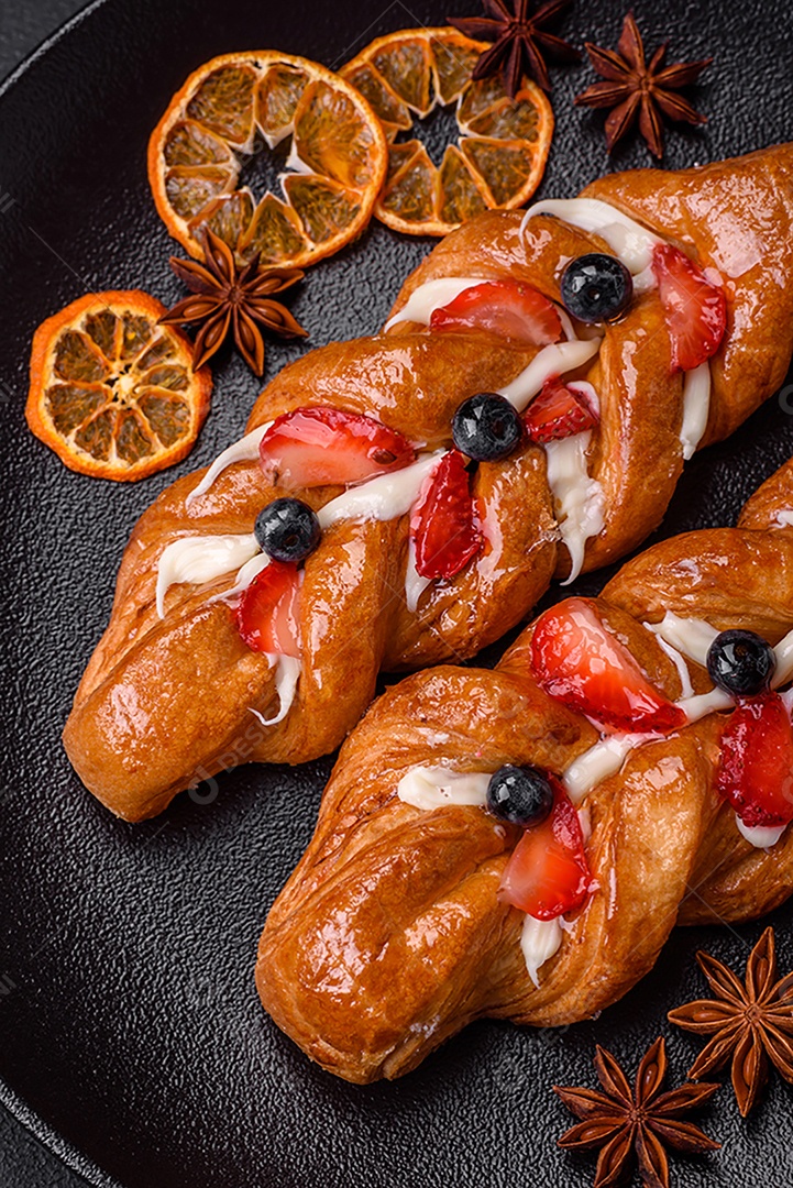 Deliciosa massa crocante fresca em forma de trança com morangos e mirtilos sobre um fundo escuro de concreto