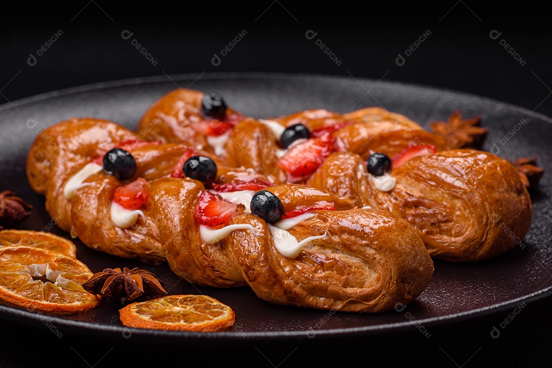 Deliciosa massa crocante fresca em forma de trança com morangos e mirtilos sobre um fundo escuro de concreto