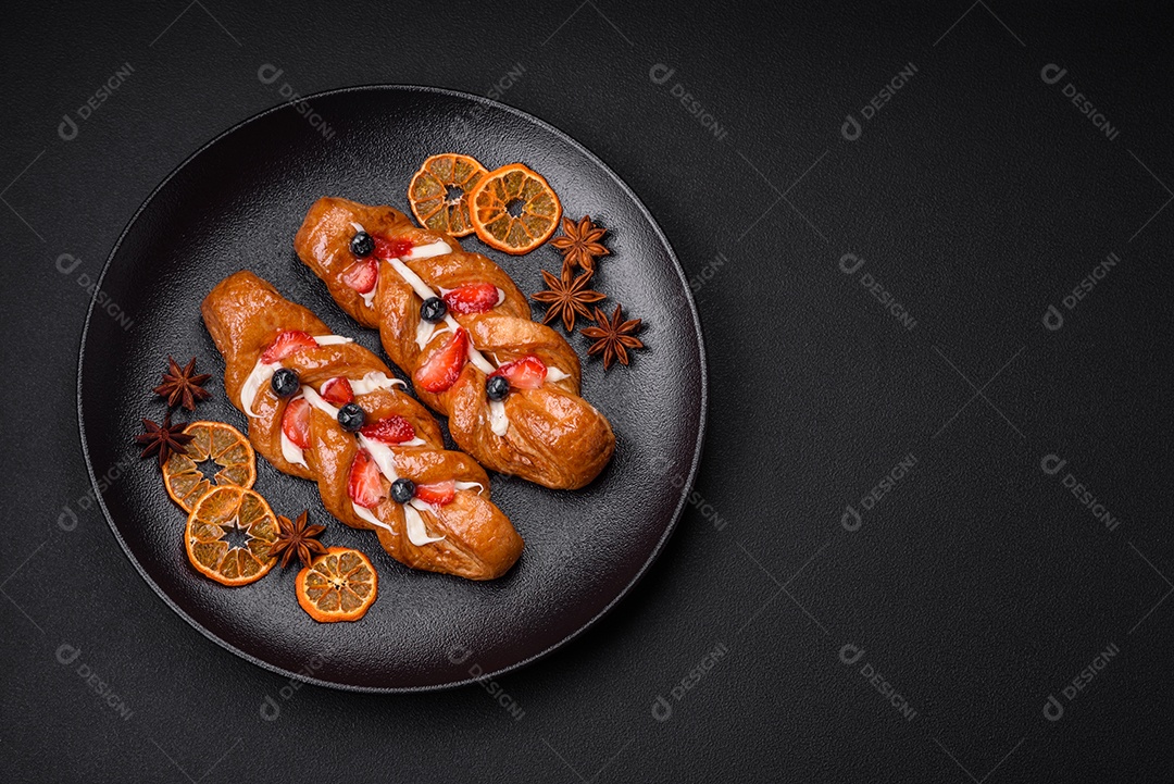 Deliciosa massa crocante fresca em forma de trança com morangos e mirtilos sobre um fundo escuro de concreto