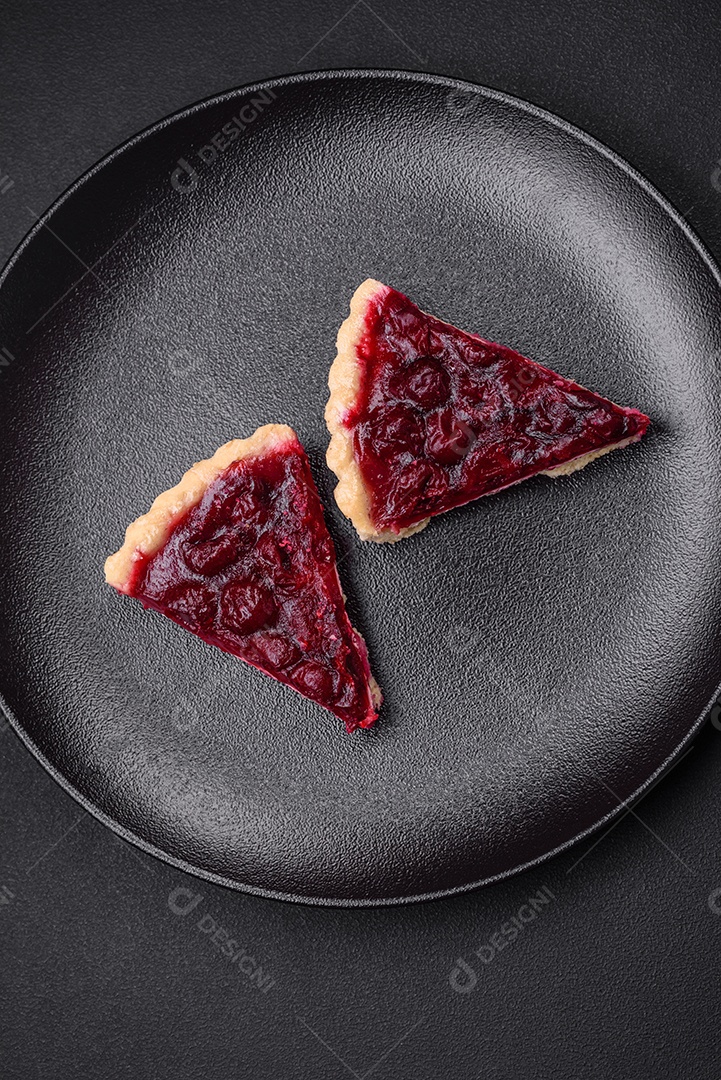 Deliciosa torta doce perfumada com bagas de cereja em uma placa de cerâmica sobre um fundo escuro de concreto