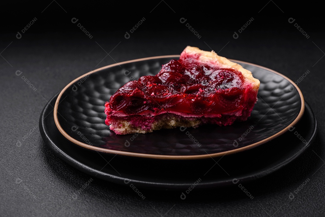 Deliciosa torta doce perfumada com bagas de cereja em uma placa de cerâmica sobre um fundo escuro de concreto