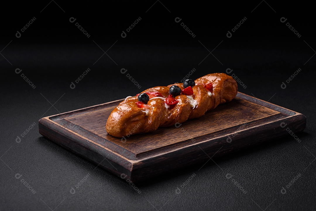 Deliciosa massa crocante fresca em forma de trança com morangos e mirtilos sobre um fundo escuro de concreto