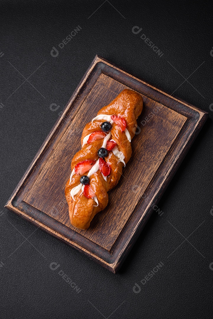 Deliciosa massa crocante fresca em forma de trança com morangos e mirtilos sobre um fundo escuro de concreto