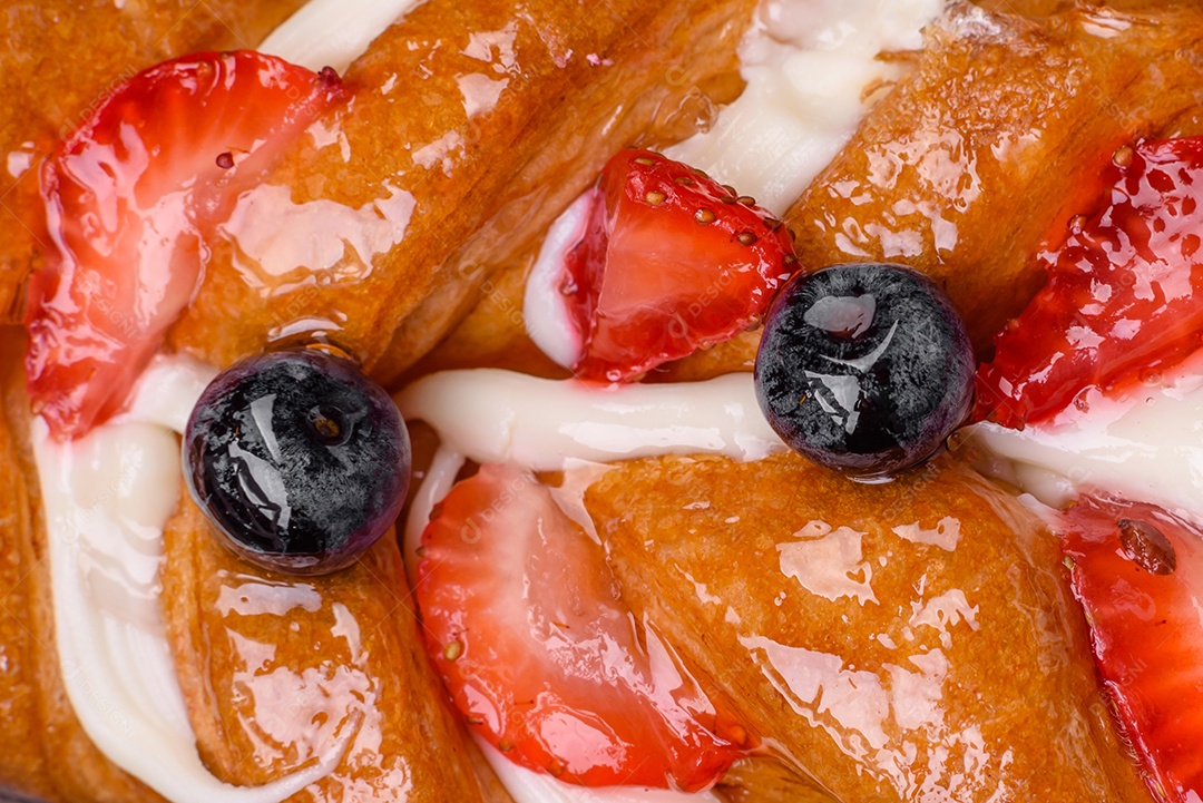 Deliciosa massa crocante fresca em forma de trança com morangos e mirtilos sobre um fundo escuro de concreto