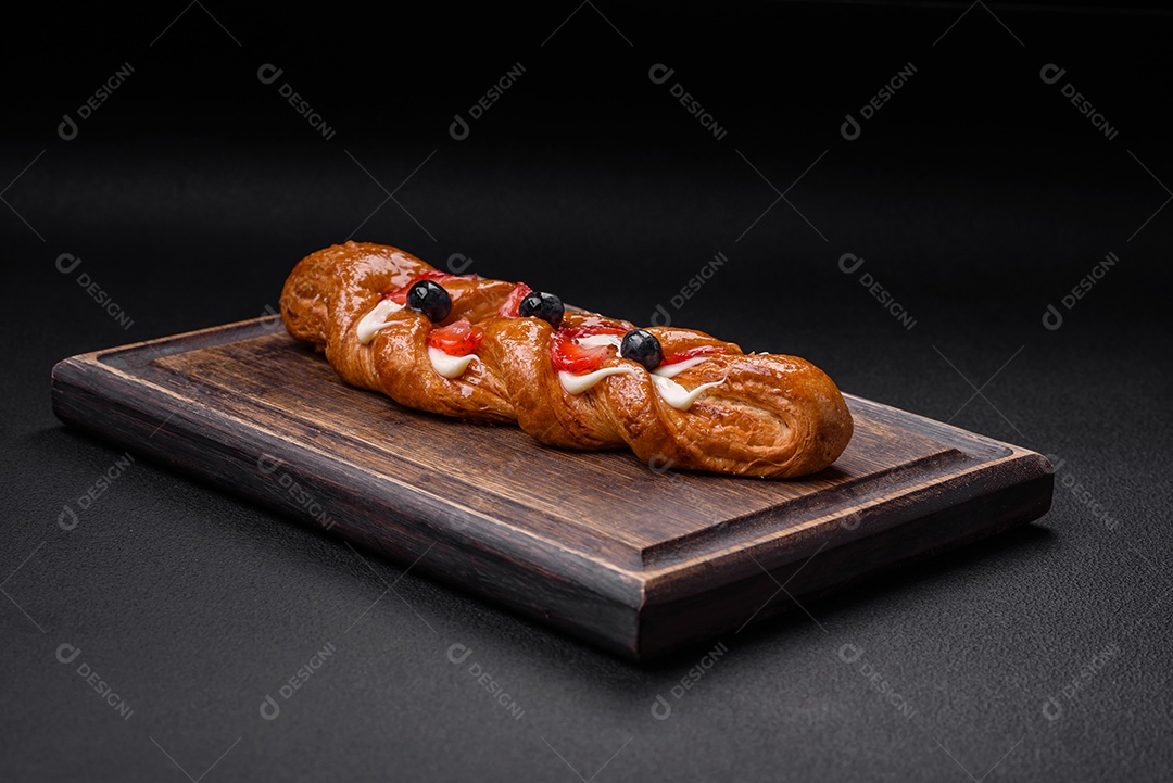 Deliciosa massa crocante fresca em forma de trança com morangos e mirtilos sobre um fundo escuro de concreto