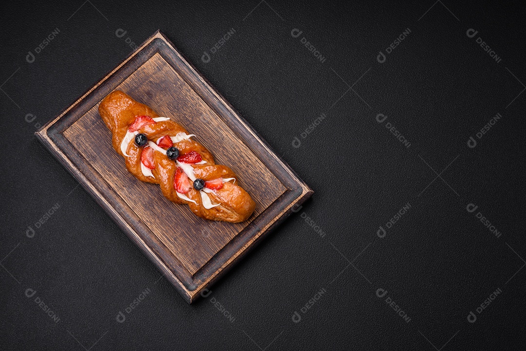Deliciosa massa crocante fresca em forma de trança com morangos e mirtilos sobre um fundo escuro de concreto