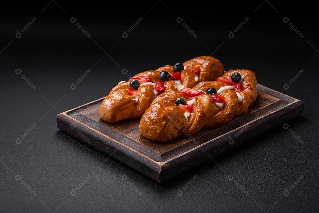 Deliciosa massa crocante fresca em forma de trança com morangos e mirtilos sobre um fundo escuro de concreto