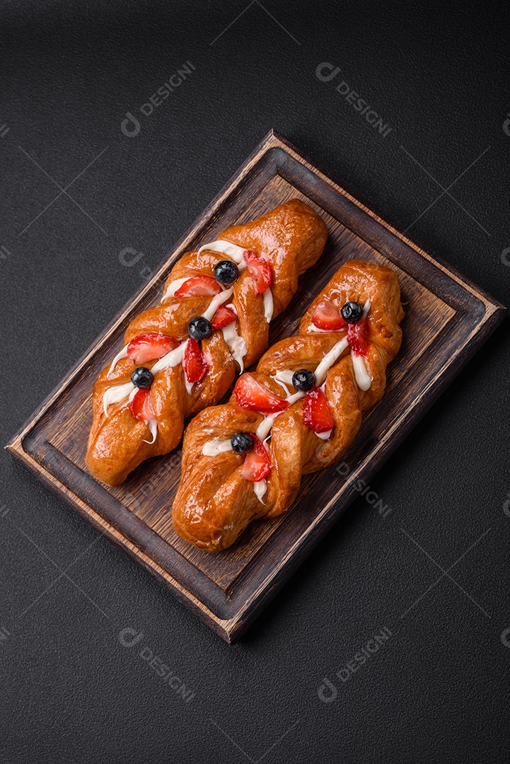 Deliciosa massa crocante fresca em forma de trança com morangos e mirtilos sobre um fundo escuro de concreto