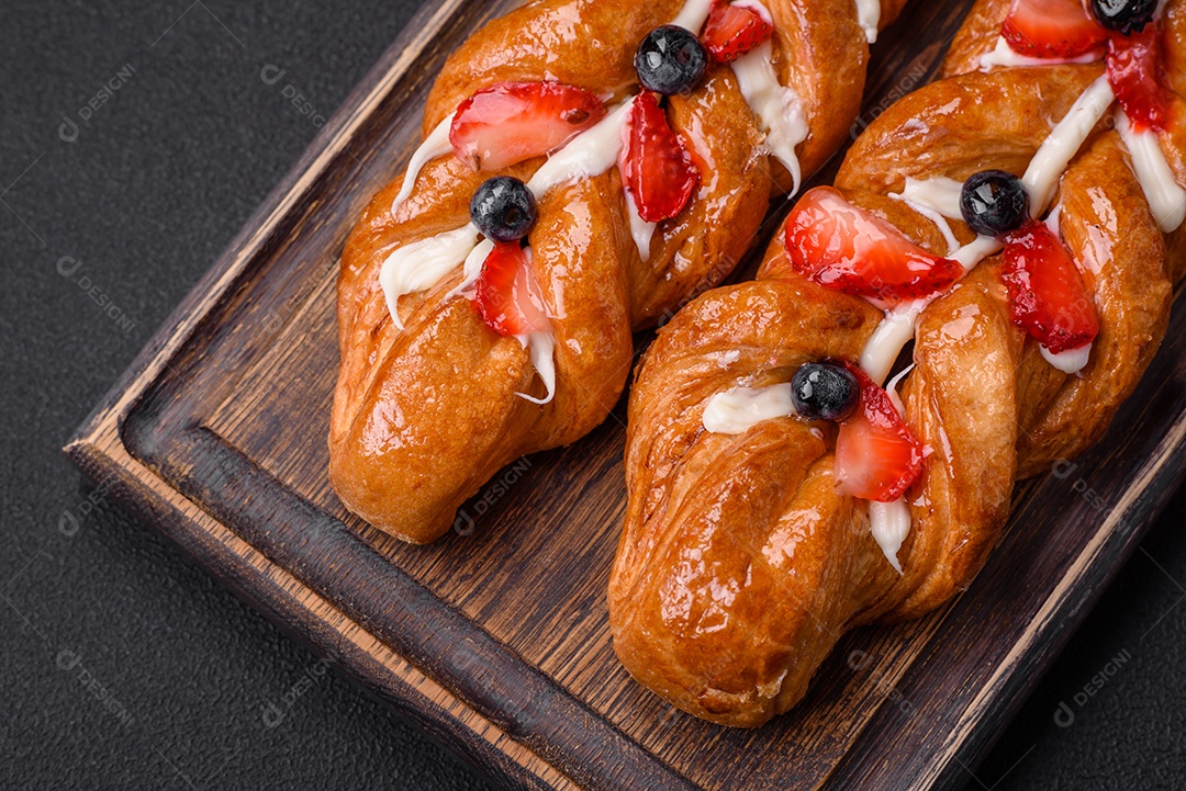 Deliciosa massa crocante fresca em forma de trança com morangos e mirtilos sobre um fundo escuro de concreto