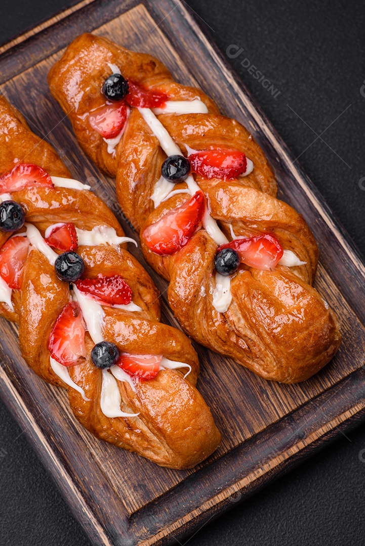 Deliciosa massa crocante fresca em forma de trança com morangos e mirtilos sobre um fundo escuro de concreto