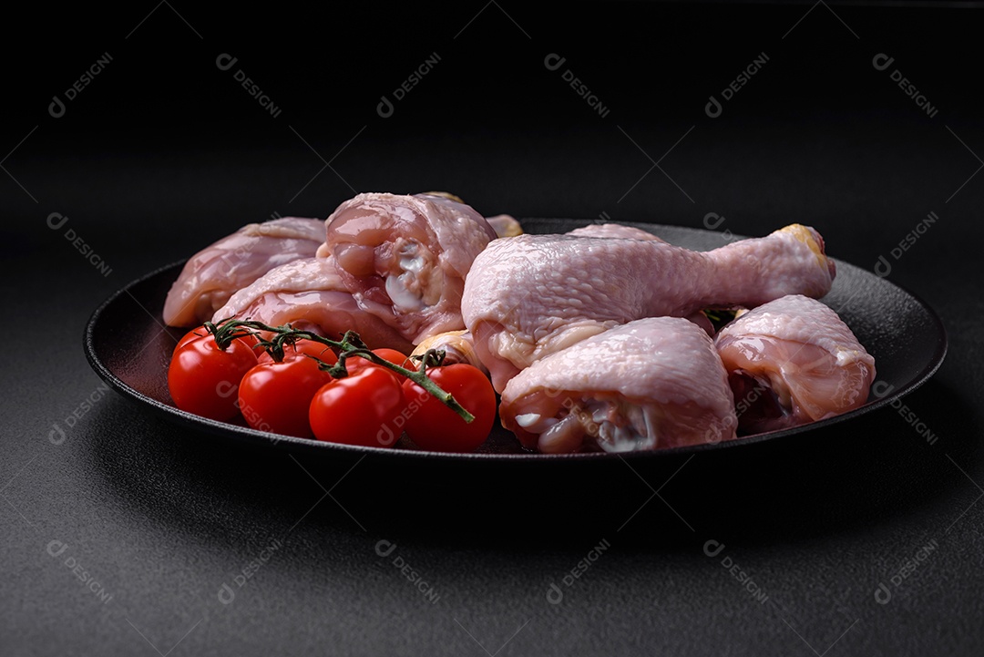 Pernas de frango cru com sal, especiarias e ervas sobre um fundo escuro de concreto