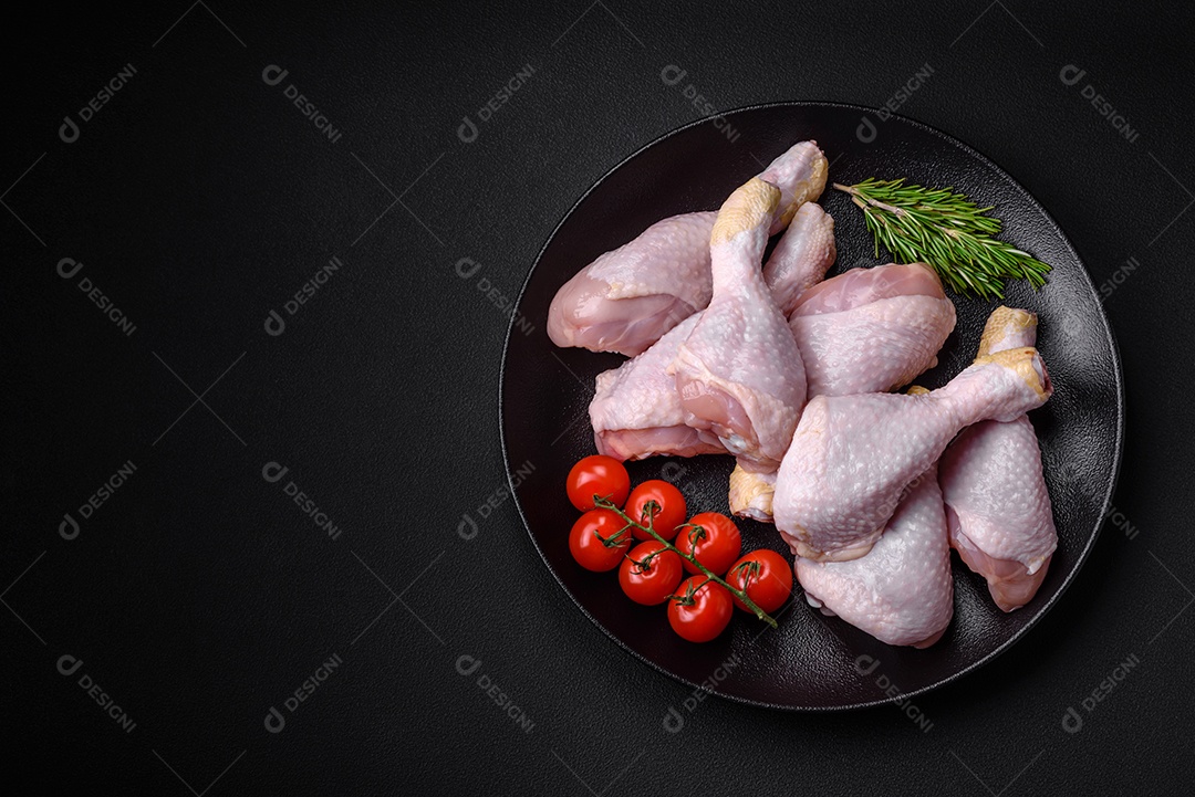 Pernas de frango cru com sal, especiarias e ervas sobre um fundo escuro de concreto