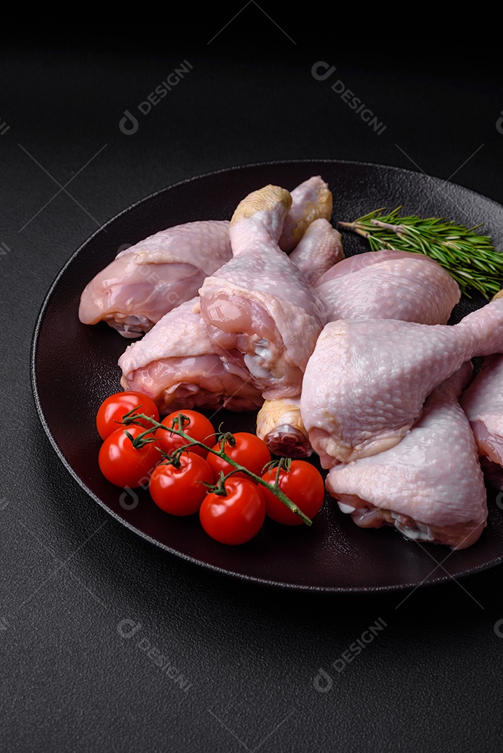 Pernas de frango cru com sal, especiarias e ervas sobre um fundo escuro de concreto