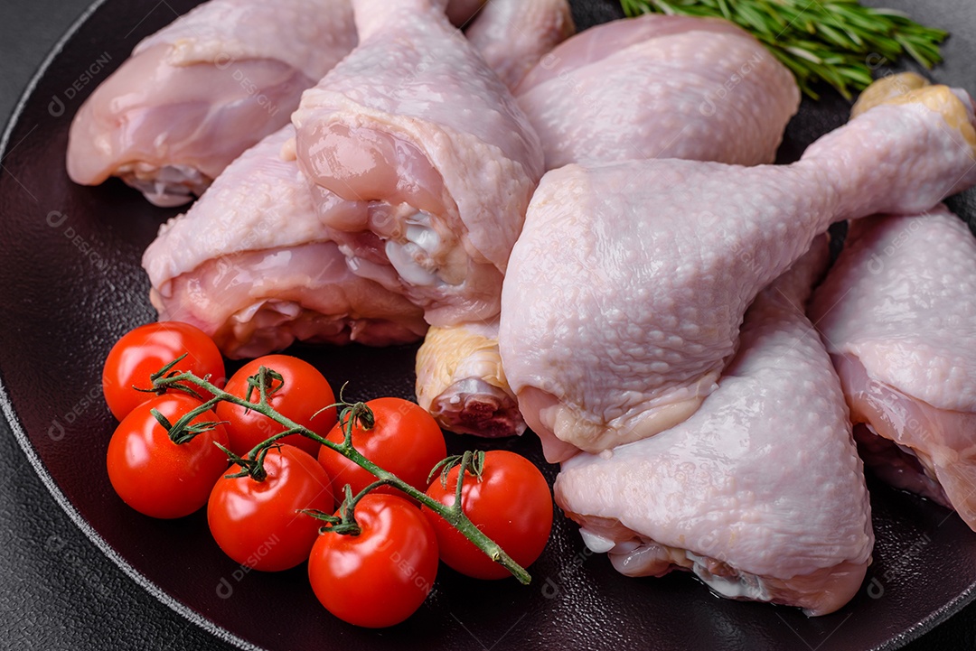 Pernas de frango cru com sal, especiarias e ervas sobre um fundo escuro de concreto