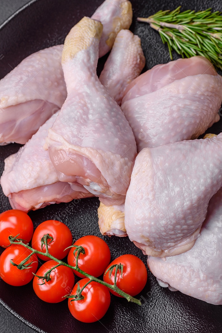 Pernas de frango cru com sal, especiarias e ervas sobre um fundo escuro de concreto