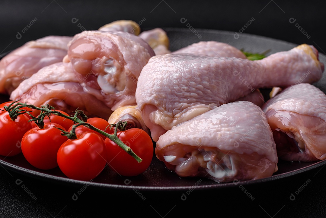 Pernas de frango cru com sal, especiarias e ervas sobre um fundo escuro de concreto