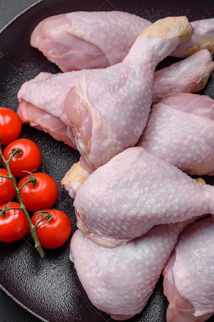 Pernas de frango cru com sal, especiarias e ervas sobre um fundo escuro de concreto