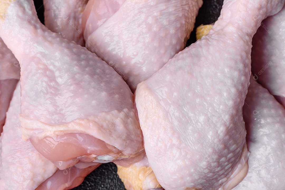 Pernas de frango cru com sal, especiarias e ervas sobre um fundo escuro de concreto