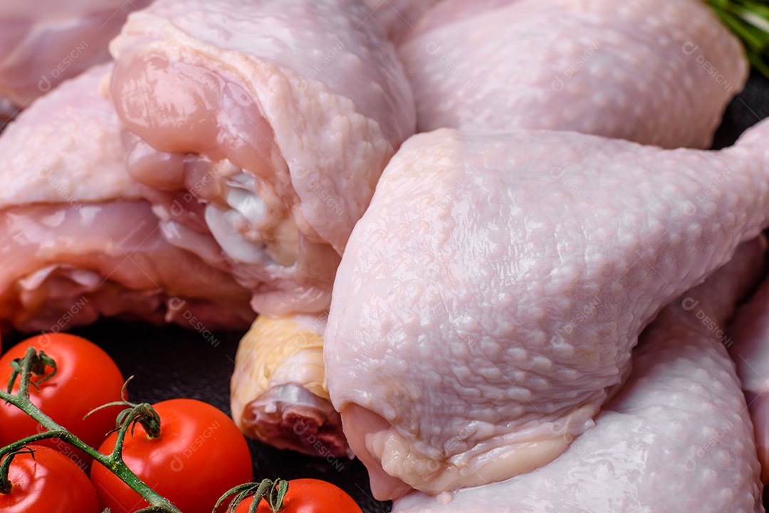 Pernas de frango cru com sal, especiarias e ervas sobre um fundo escuro de concreto