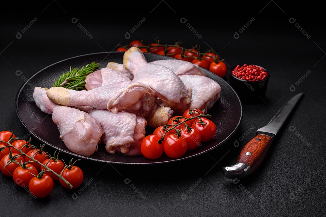 Pernas de frango cru com sal, especiarias e ervas sobre um fundo escuro de concreto