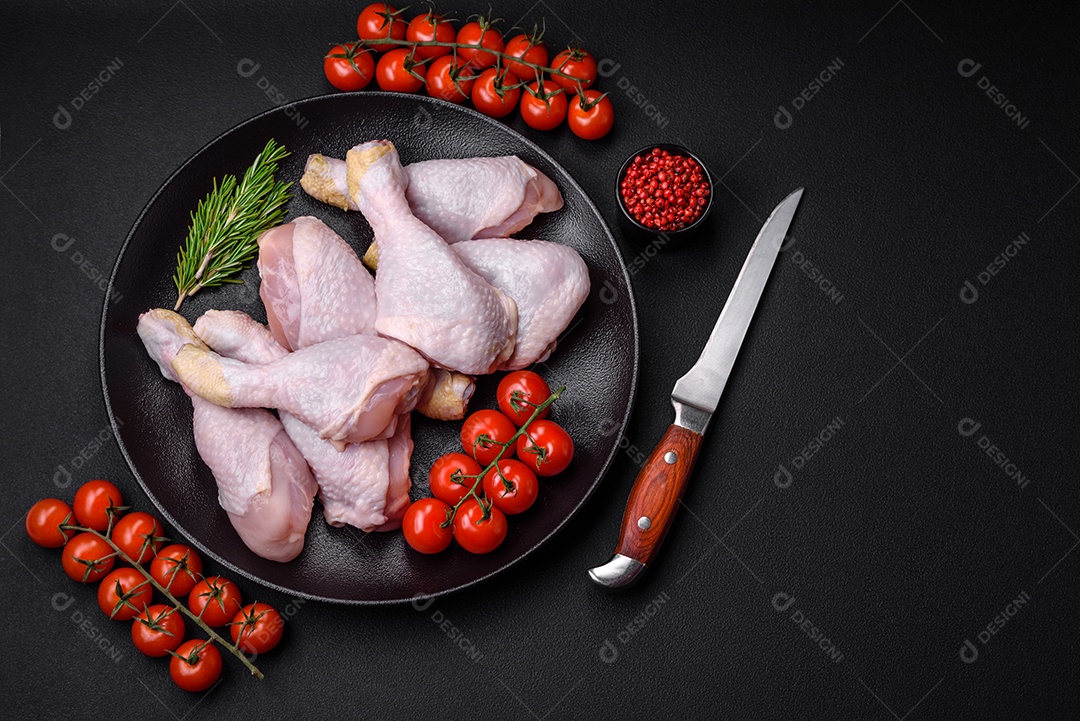 Pernas de frango cru com sal, especiarias e ervas sobre um fundo escuro de concreto