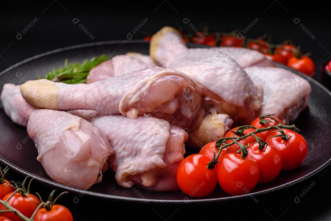 Pernas de frango cru com sal, especiarias e ervas sobre um fundo escuro de concreto