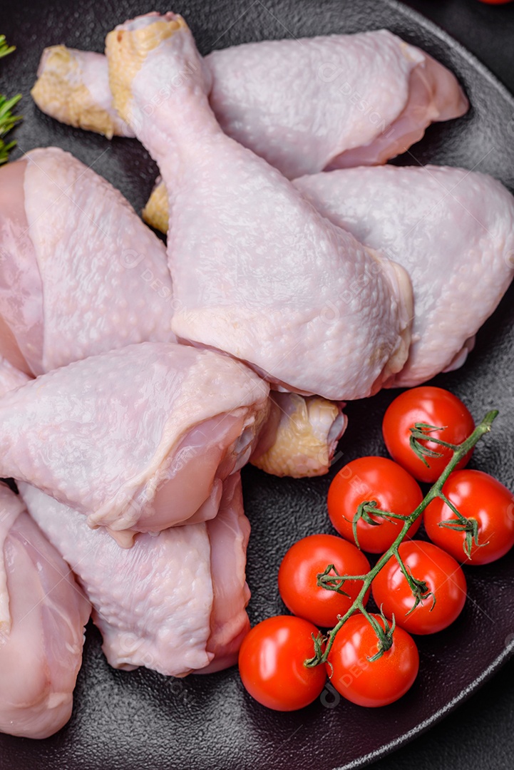 Pernas de frango cru com sal, especiarias e ervas sobre um fundo escuro de concreto