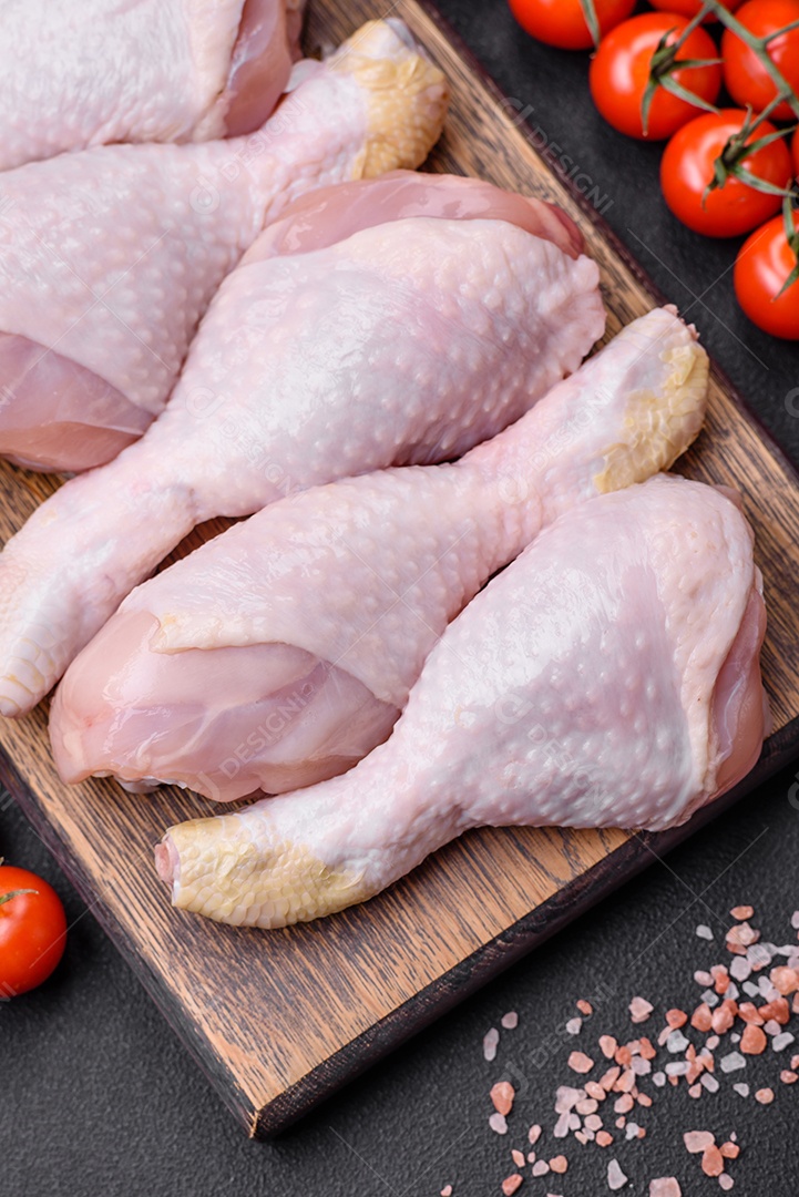 Pernas de frango cru com sal, especiarias e ervas sobre um fundo escuro de concreto