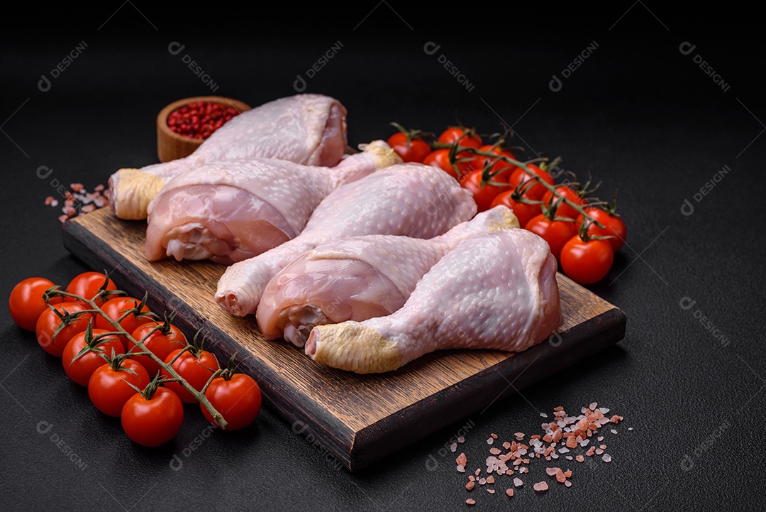 Pernas de frango cru com sal, especiarias e ervas sobre um fundo escuro de concreto