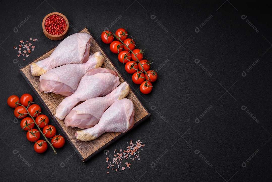 Pernas de frango cru com sal, especiarias e ervas sobre um fundo escuro de concreto