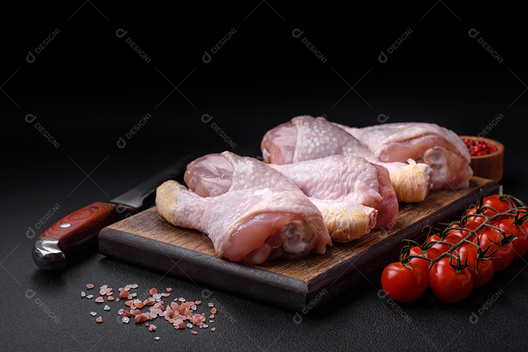 Pernas de frango cru com sal, especiarias e ervas sobre um fundo escuro de concreto