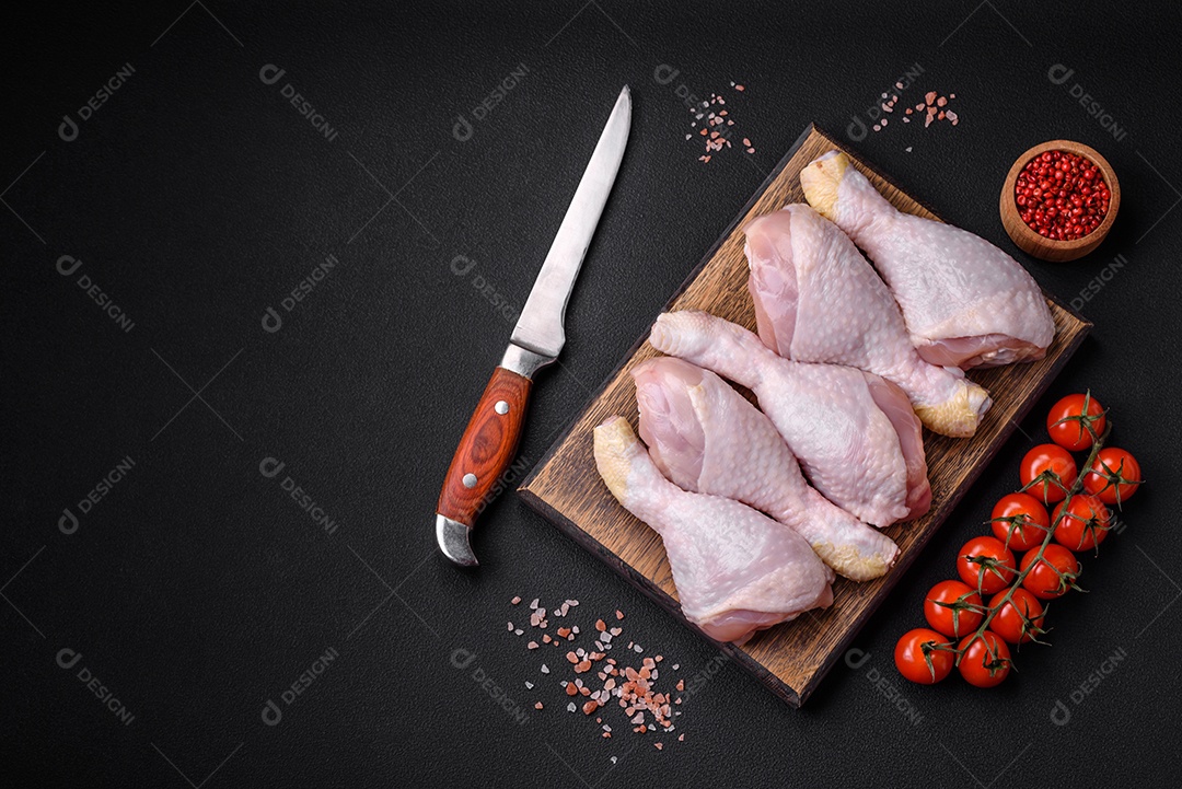 Pernas de frango cru com sal, especiarias e ervas sobre um fundo escuro de concreto