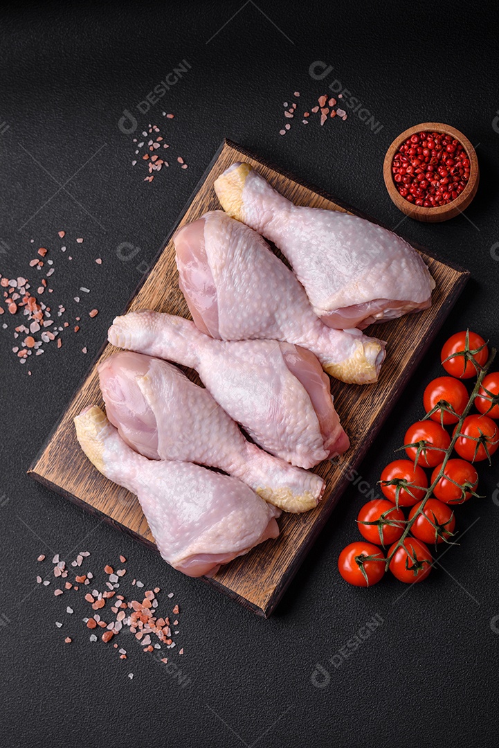 Pernas de frango cru com sal, especiarias e ervas sobre um fundo escuro de concreto