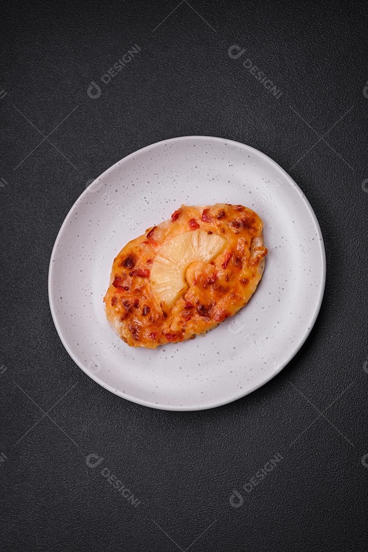 Filé de frango grelhado em forma de bife com tomate, abacaxi e queijo sobre fundo escuro de concreto