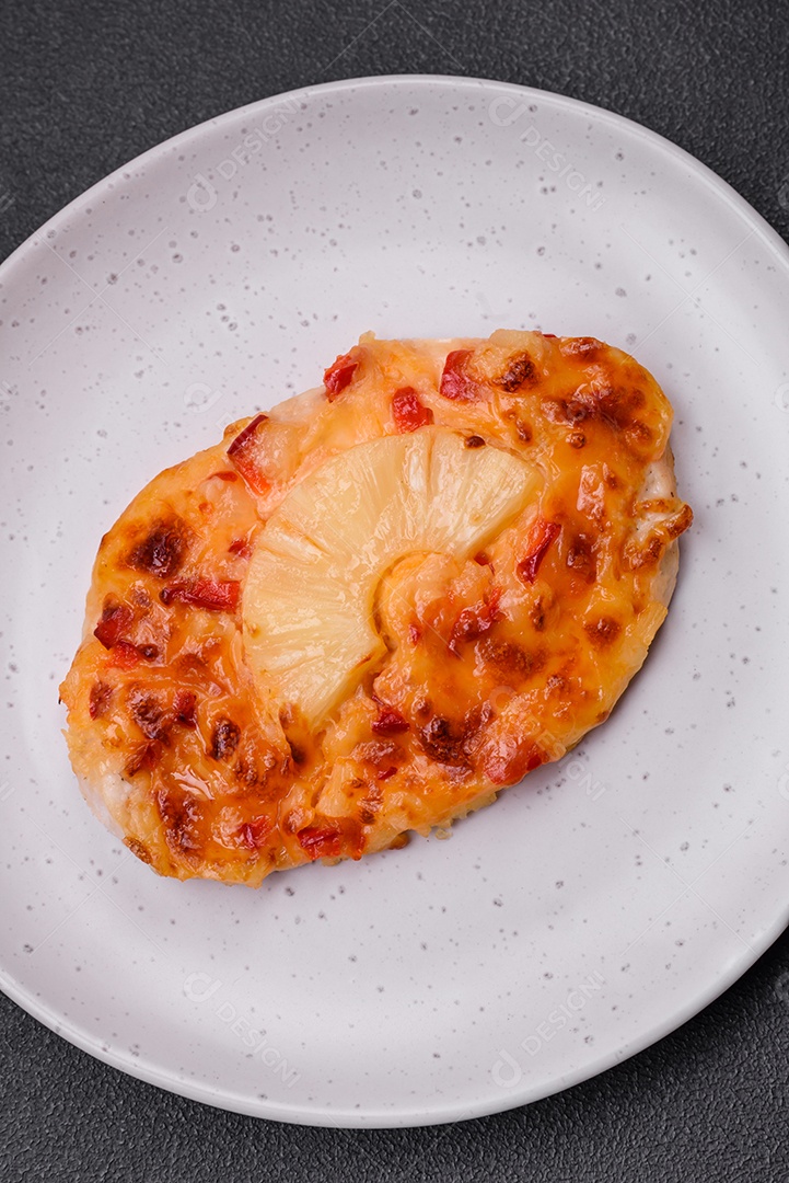 Filé de frango grelhado em forma de bife com tomate, abacaxi e queijo sobre fundo escuro de concreto