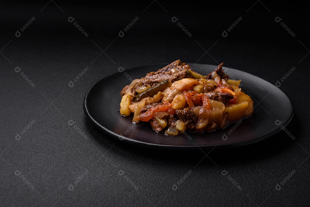 Delicioso ensopado com batatas, tomates, carne, cebolas e cenouras num prato cerâmico sobre um fundo escuro de concreto