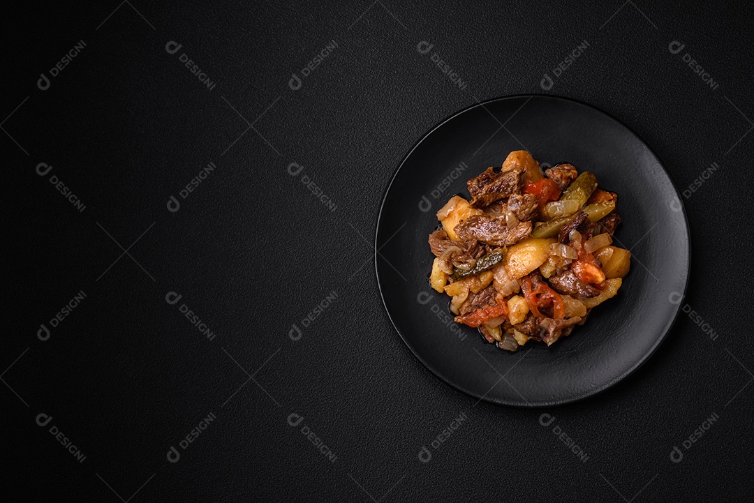 Delicioso ensopado com batatas, tomates, carne, cebolas e cenouras num prato cerâmico sobre um fundo escuro de concreto